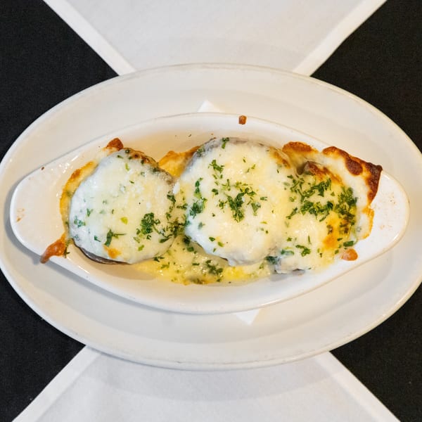 Three portions of a cheesy baked dish topped with fresh parsley in an oval white serving dish.