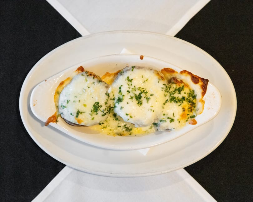 Three portions of a cheesy baked dish topped with fresh parsley in an oval white serving dish.