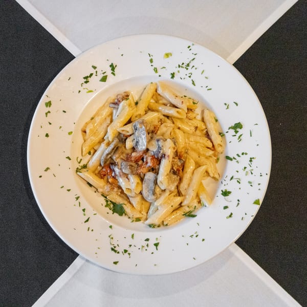 White plate of creamy penne pasta with mushrooms, bacon, and fresh parsley.