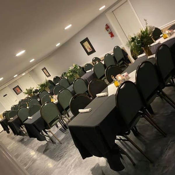 A long, narrow banquet hall with rows of tables draped in black, set with white runners and floral centerpieces.
