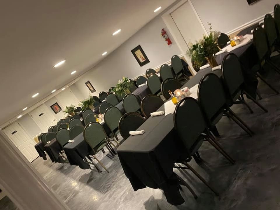 A long, narrow banquet hall with rows of tables draped in black, set with white runners and floral centerpieces.