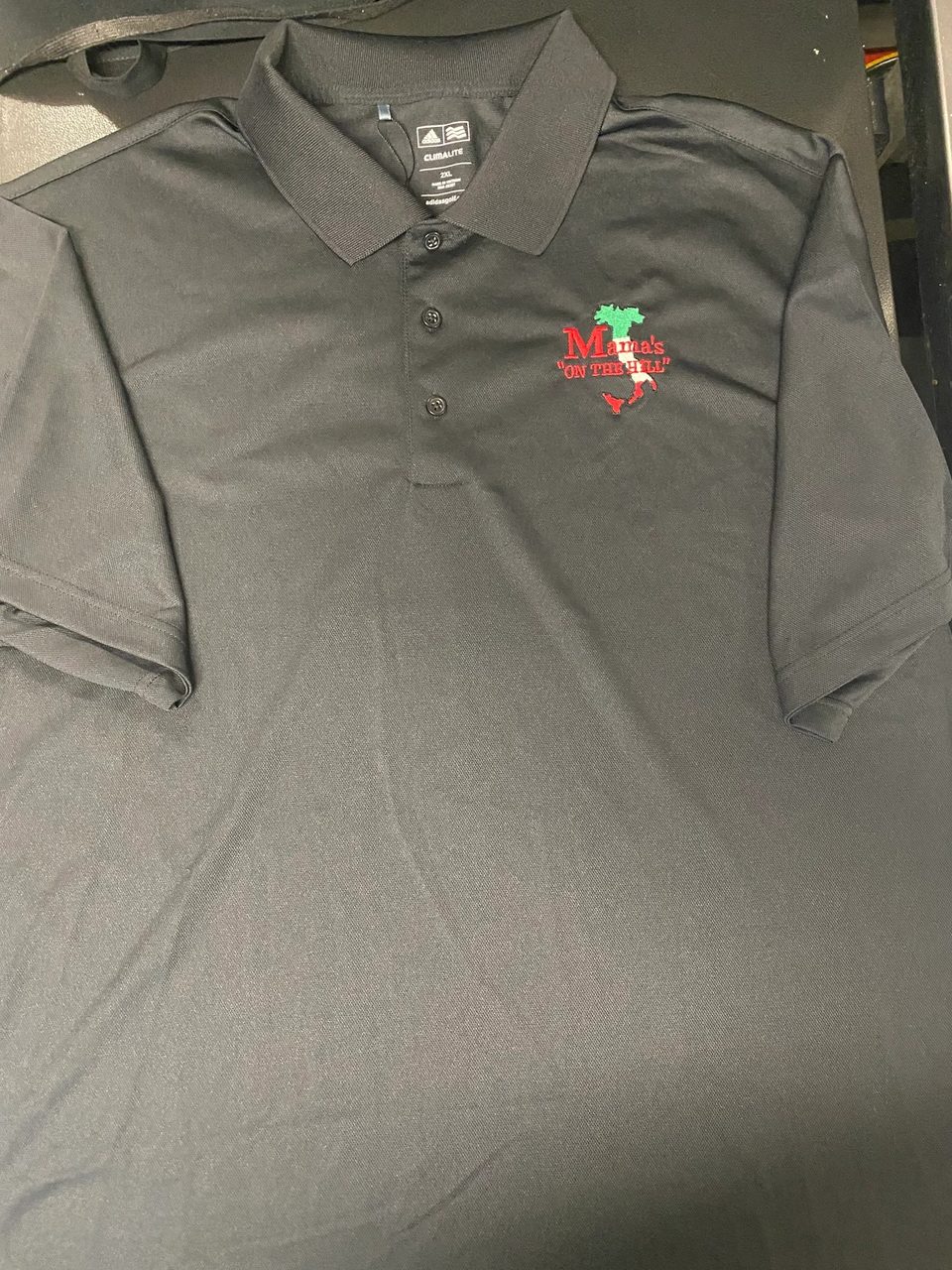 Black polo shirt with "Mama's ON THE HILL" logo featuring the Italian flag colors.