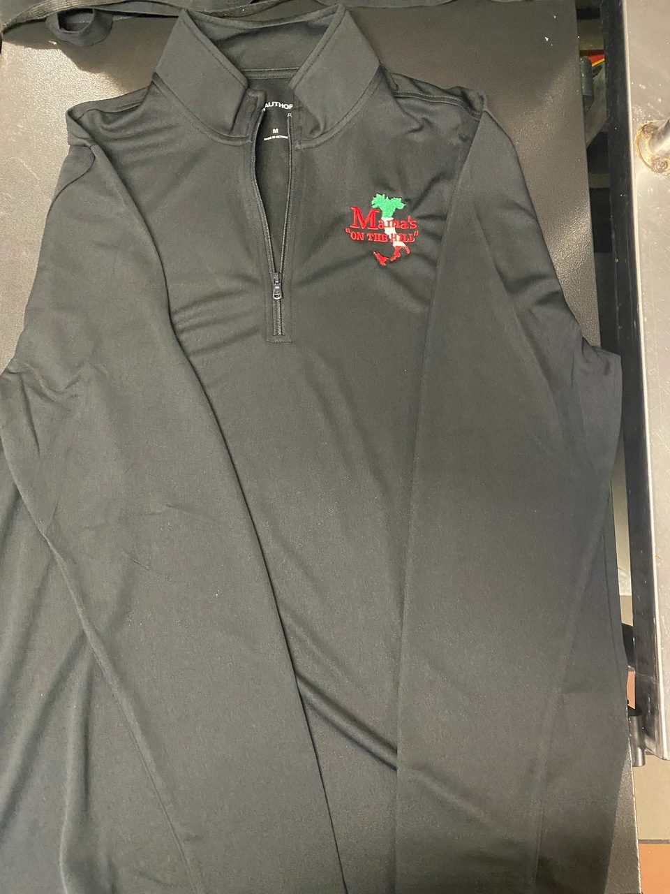 Black long-sleeved shirt with a zipper, featuring the "Mama's On The Hill" logo.