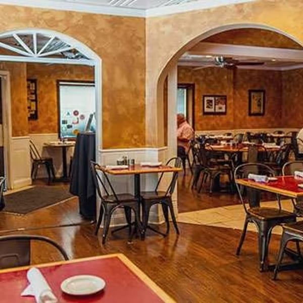 Warmly lit restaurant interior with arched doorways, red-topped tables, and dark chairs, with patrons dining.