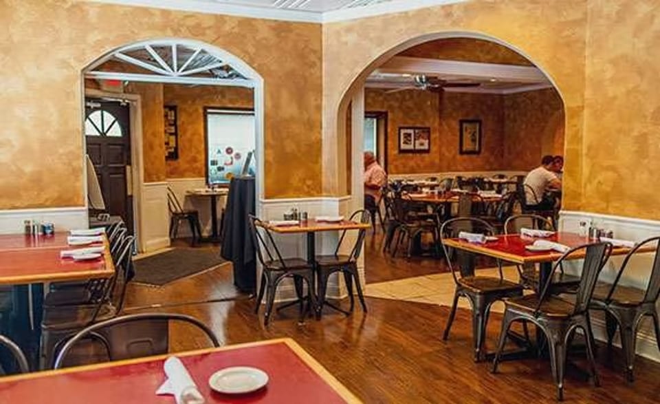Warmly lit restaurant interior with arched doorways, red-topped tables, and dark chairs, with patrons dining.