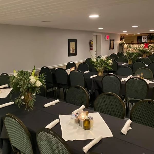A banquet room with rows of tables draped in black, set with white napkins, candles, and floral centerpieces.