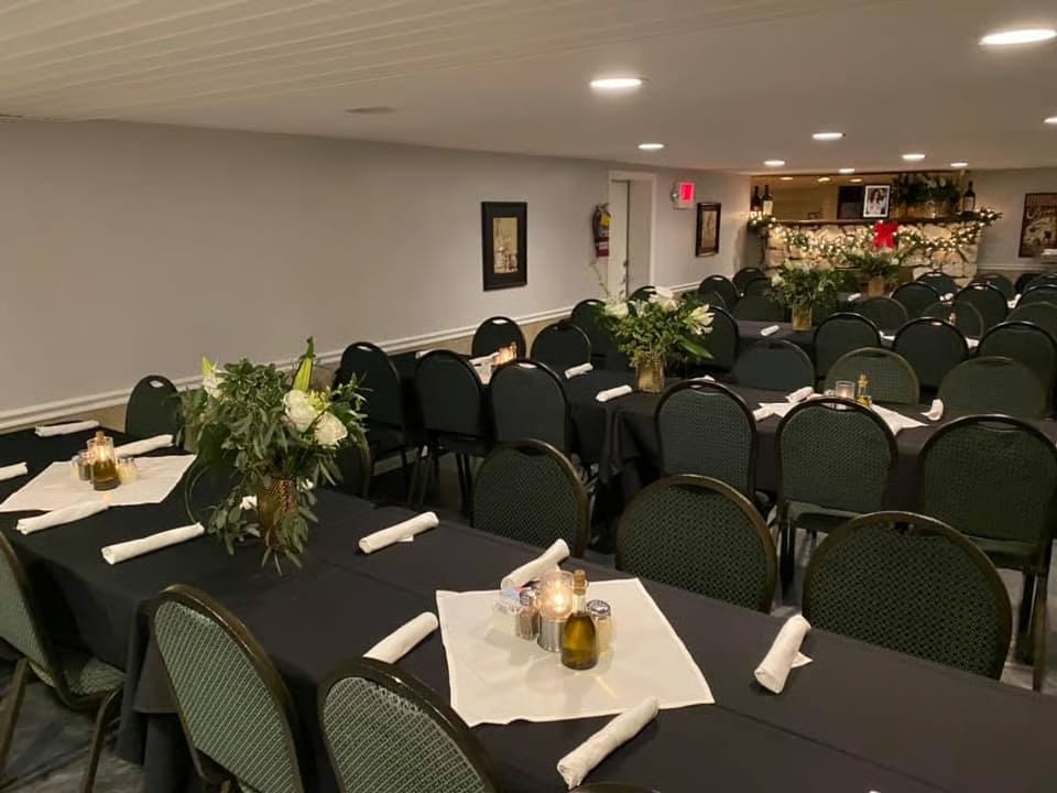 A banquet room with rows of tables draped in black, set with white napkins, candles, and floral centerpieces.