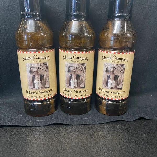 Three bottles of Mama Campisi's Balsamic Vinaigrette with vintage labels on a black surface.