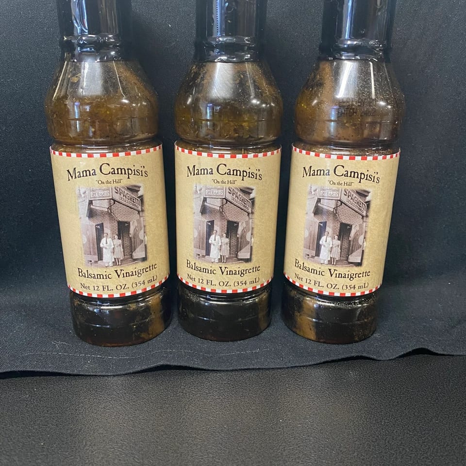 Three bottles of Mama Campisi's Balsamic Vinaigrette with vintage labels on a black surface.