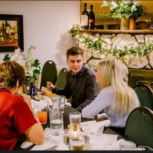 Four people dining at a restaurant table with a stone fireplace and festive garland in the background.