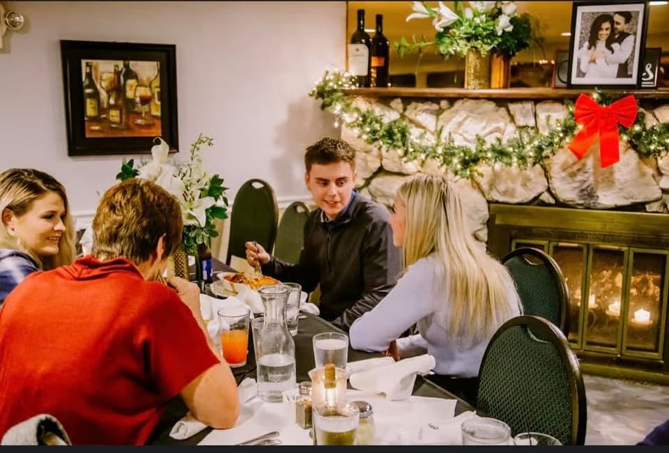 Four people dining at a restaurant table with a stone fireplace and festive garland in the background.