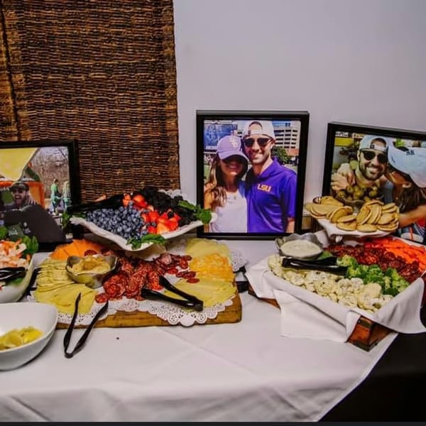 A buffet table with shrimp, fruit, cheese, meats, and vegetables, with framed photos behind the food.