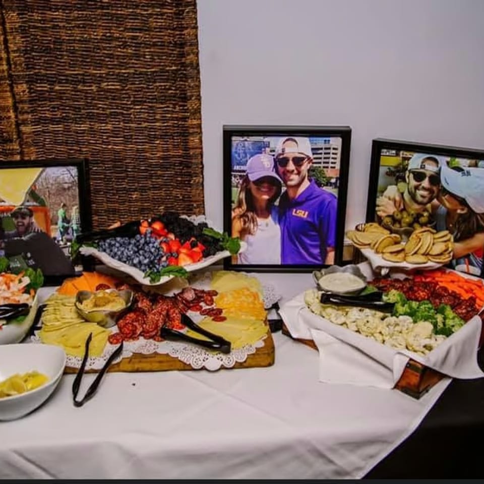 A buffet table with shrimp, fruit, cheese, meats, and vegetables, with framed photos behind the food.