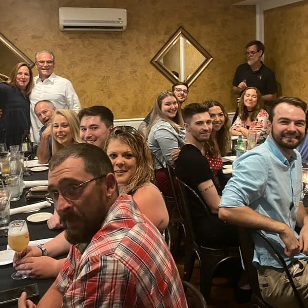 A large group of smiling people gathered around a long table in a restaurant, enjoying a meal.
