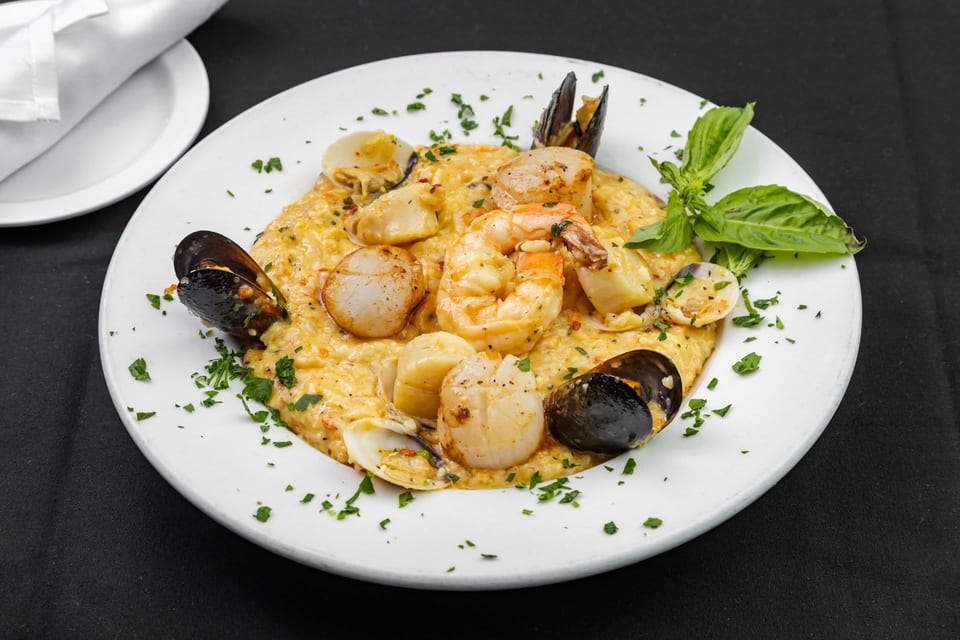 Creamy seafood risotto with mussels, scallops, shrimp, and clams, garnished with basil and parsley.