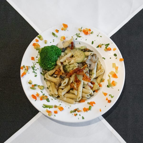 Penne pasta with broccoli, zucchini, mushrooms, sun-dried tomatoes, and bell peppers on a white plate.
