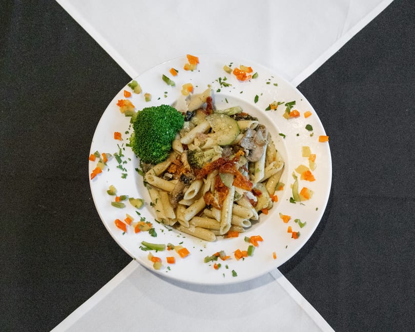 Penne pasta with broccoli, zucchini, mushrooms, sun-dried tomatoes, and bell peppers on a white plate.