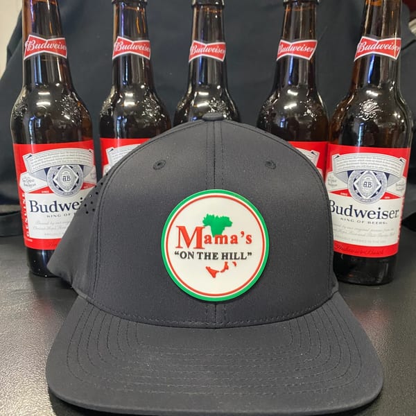 Black Mama's "ON THE HILL" baseball cap in front of five Budweiser beer bottles.