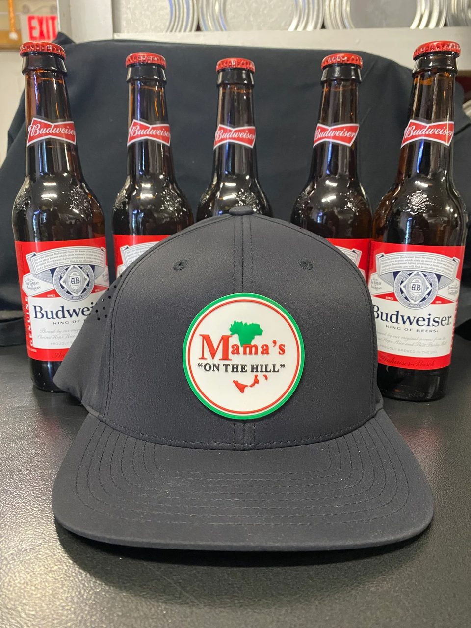 Black Mama's "ON THE HILL" baseball cap in front of five Budweiser beer bottles.
