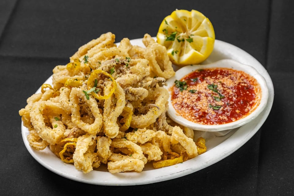 Crispy fried calamari with lemon wedges and a side of marinara sauce on a white plate.