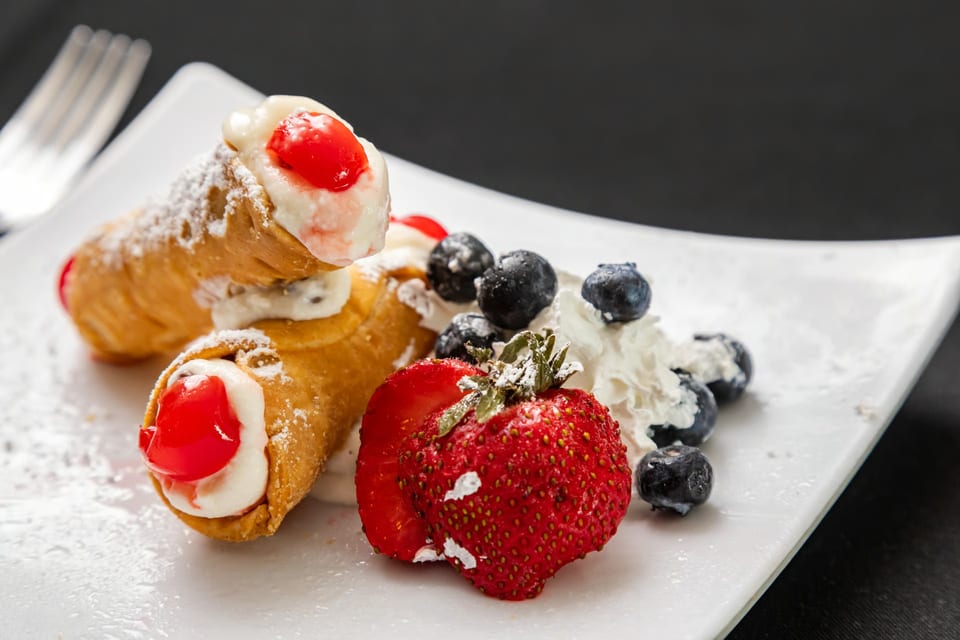 Two cannolis with cherries, whipped cream, blueberries, and a strawberry on a white plate.